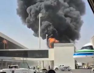 Smoke and flames rise beside an airport terminal as an airliner stands at a gate